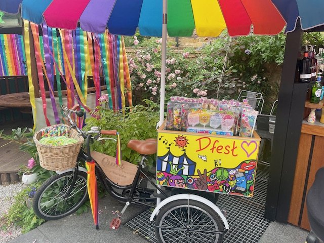 A beautiful bike-cart set up with goodies for DFest. There is a colourful parasol, flowers and streamers in the background.